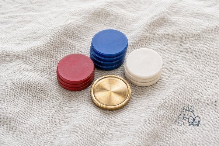 一枚黄铜庄家按钮与三叠高低不同的素面筹码围成弧形,正俯拍